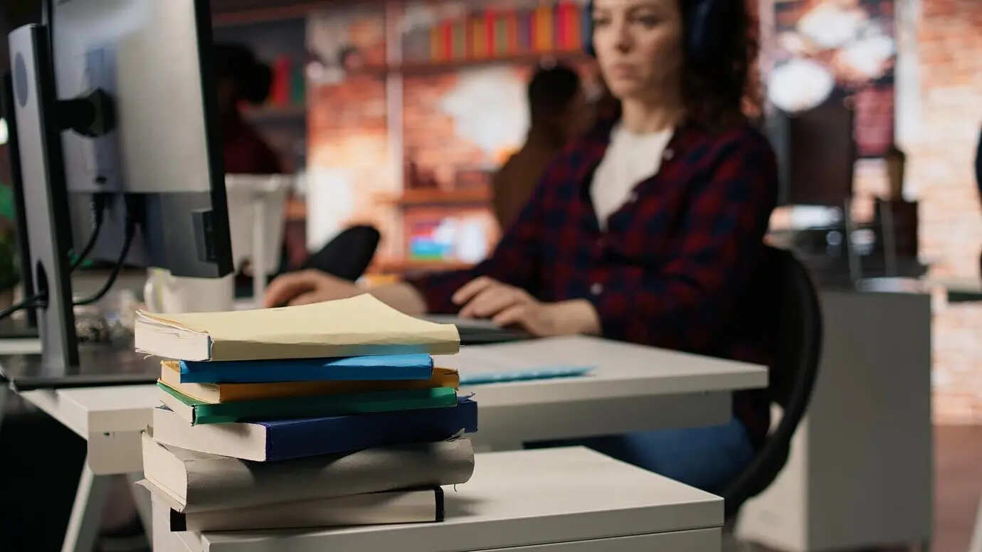 Стопка книг на рабочем столе в офисе стартапа перед работающей женщиной, крупный план.